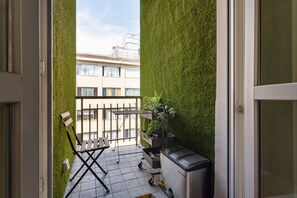 Ein Balkon mit grüner Wand, einem Klappsessel, einem kleinen Tisch und einer kompakten Küchenzeile.