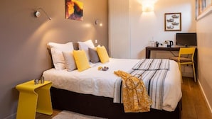 Un dormitorio con cama, mesita de noche, escritorio, silla y una obra de arte.