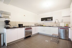 A modern kitchen with white cabinets, a stainless steel dishwasher, a gas stove, and a coffee machine. - La Maison de Karen Chocolat (Limonest)