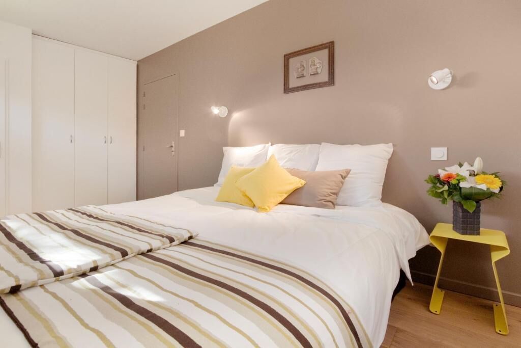 Un dormitorio con cama, almohadas, una mesita de noche con un florero y un armario.