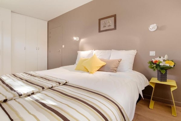 Un dormitorio con cama, almohadas, una mesita de noche con un florero y un armario.