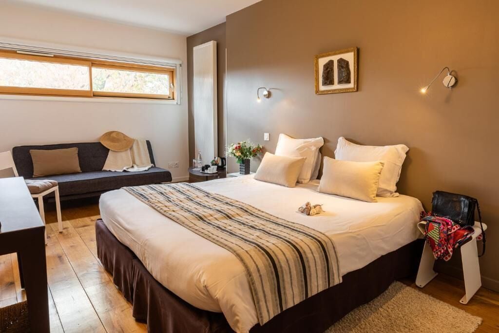 A bedroom with a large bed, a bedside table, a chair, a window, and a wall-mounted light fixture.