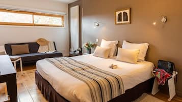 A bedroom with a large bed, a bedside table, a chair, a window, and a wall-mounted light fixture.