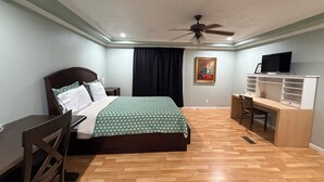 Ein Schlafzimmer mit Bett, Schreibtisch, Stuhl, Deckenventilator und Fernseher.