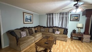 Ein Wohnzimmer mit einer Eckcouch, einem Holztisch, einem Deckenventilator und einer Lampe auf einem Beistelltisch.