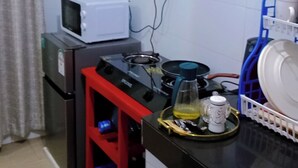 Een kleine keuken met een magnetron, fornuis en een koffieapparaat. Boven het aanrecht zijn kastjes en rechts een klein afdruiprek.