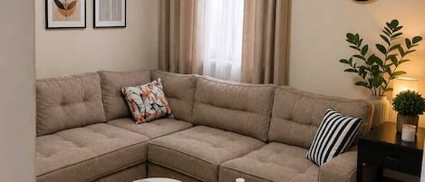 Una sala de estar con un sofá modular, dos mesas redondas de centro, un reloj de pared y una ventana con cortinas.