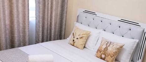 A bed with a white headboard, two pillows, a grey blanket, and two rolled towels.