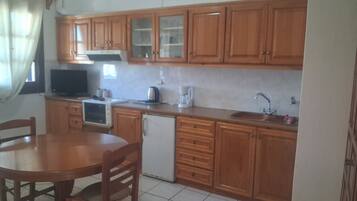 A kitchen with wooden cabinets, a refrigerator, a microwave, a sink, and a dining table with chairs.