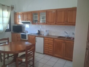 A kitchen with wooden cabinets, a refrigerator, a microwave, a sink, and a dining table with chairs. - Anastasia's 1 Apartment with Private Balcony and Sea View (Skala)