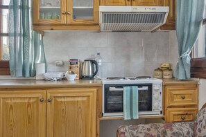 Cocina compacta con muebles de madera, horno integrado, hervidor de agua y reposa-hervidor.