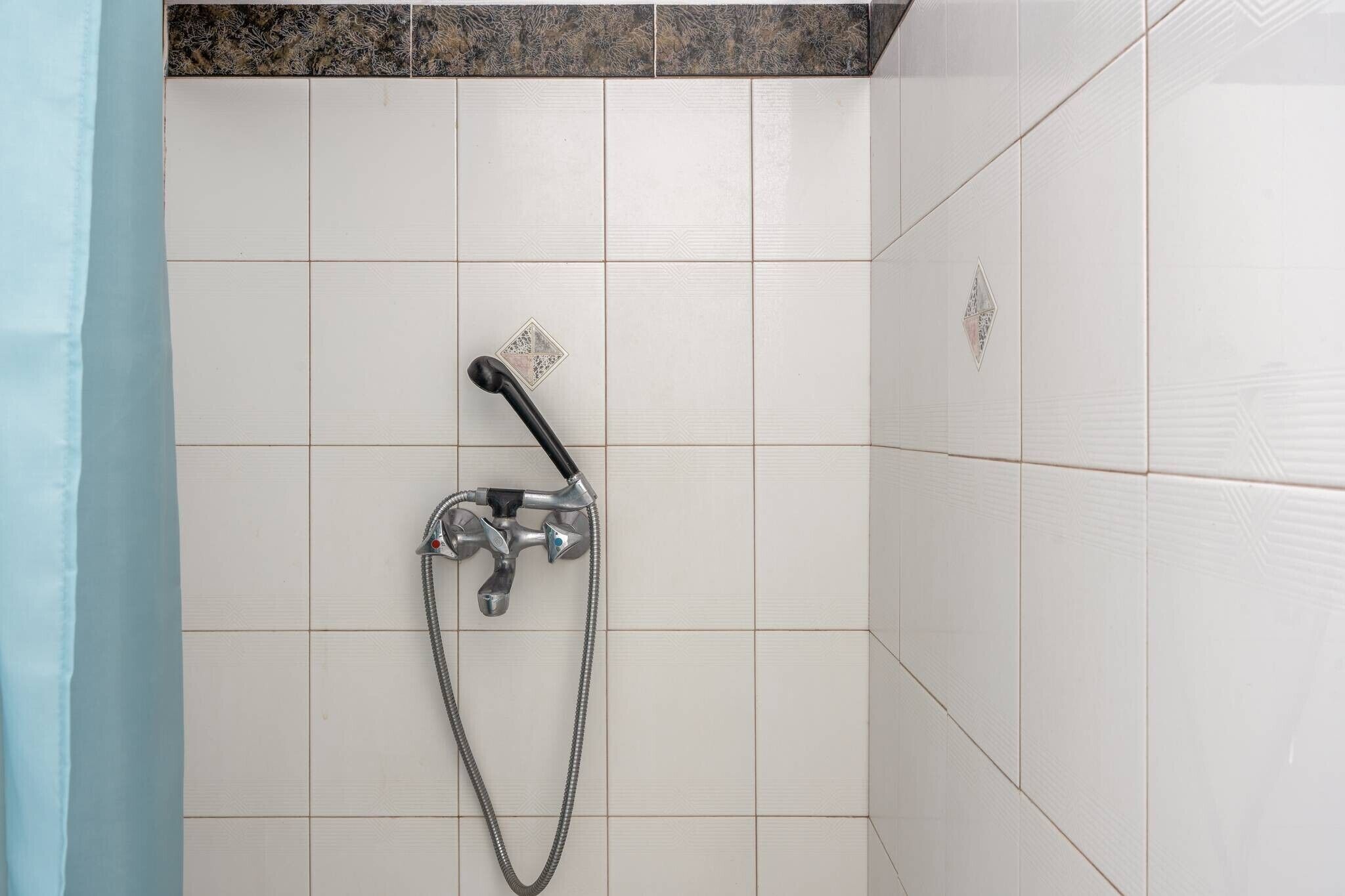 Eine Dusche mit Handbrause und flexiblen Schlauch, an einer gefliesten Wand mit Eckdesign.