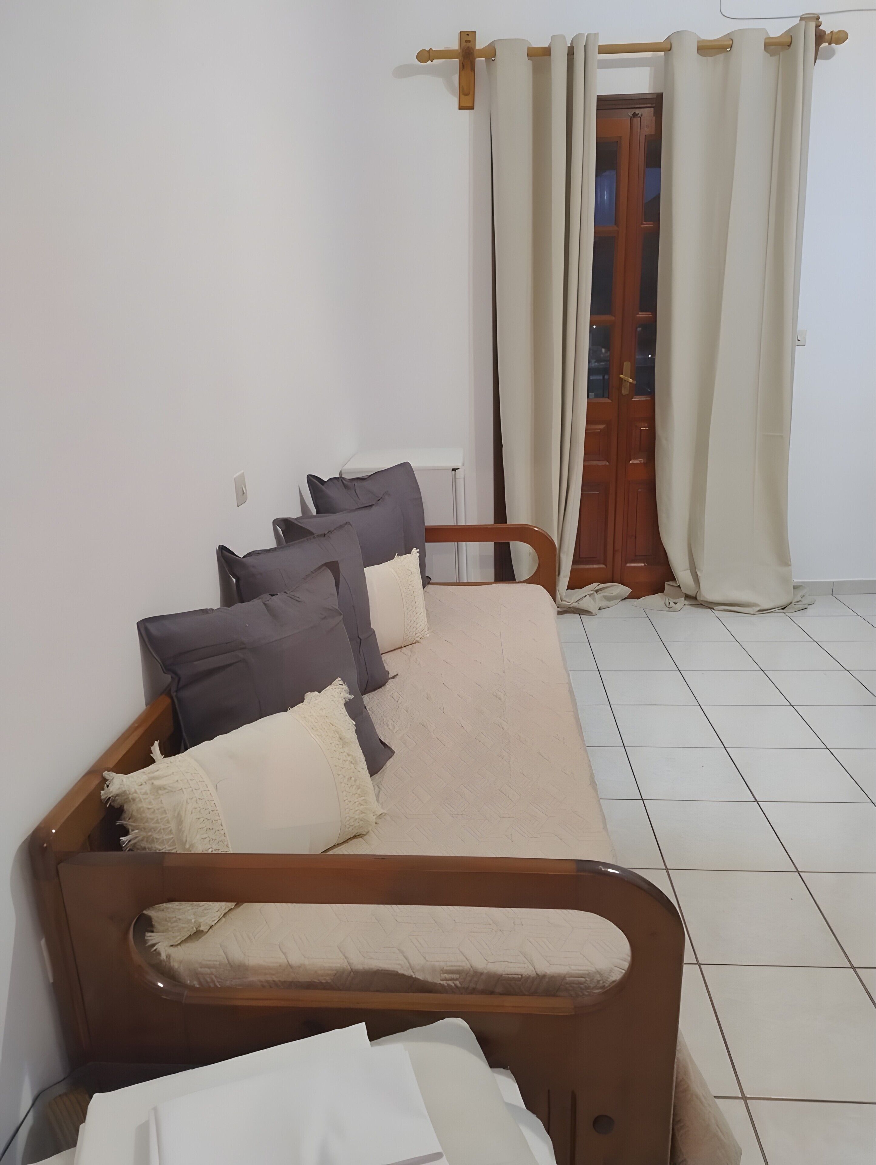 Ein Zimmer mit einem hölzernen Bett, einem weiß gefliesten Boden und einer Holztür mit Vorhang.