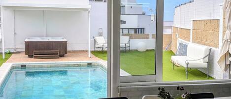 Zona junto a la piscina con una mesa y sillas, un jacuzzi y vista a un edificio residencial.