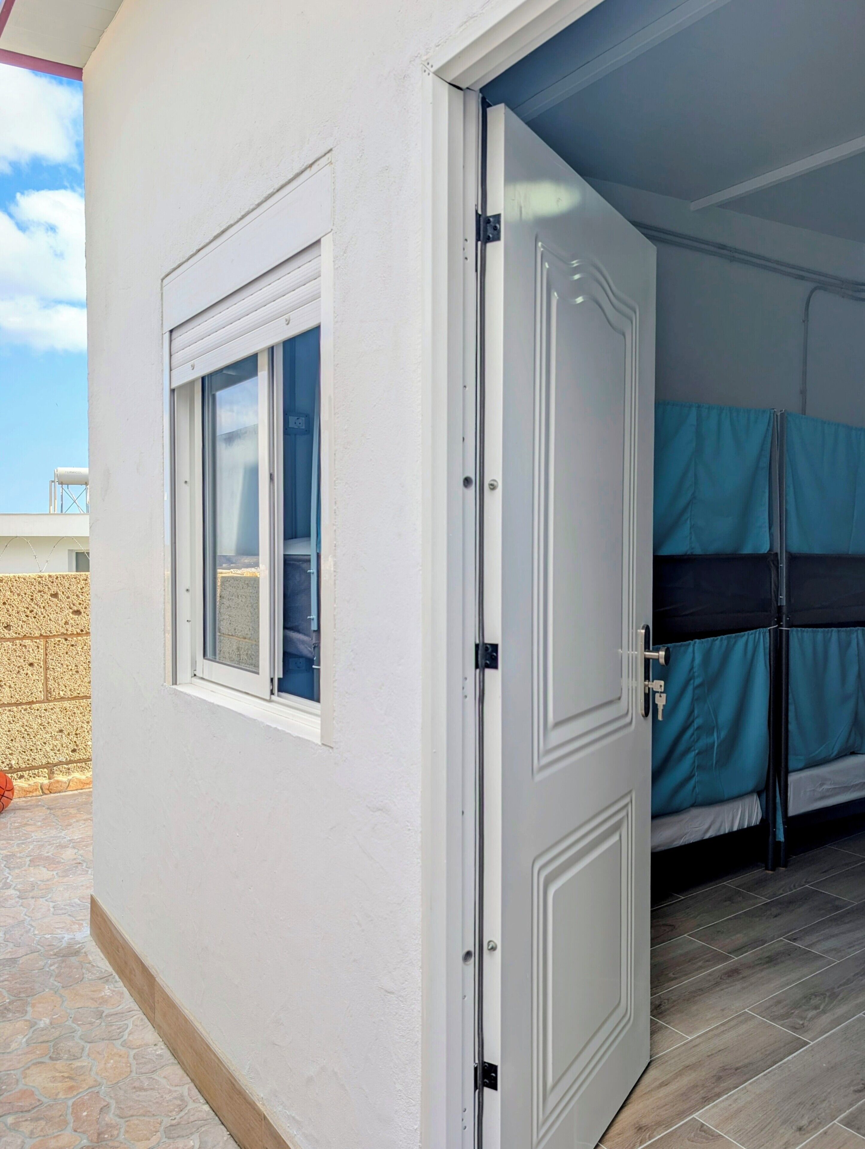 A room with a white door, a window, and a bunk bed with blue bedding.