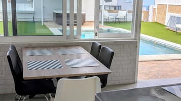 Habitación con una mesa de comedor, sillas, un ventanal y vistas a una piscina y edificios.