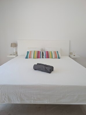 A neatly made bed with a white headboard, two pillows, a striped pillow, and a rolled-up towel on a white bedspread.