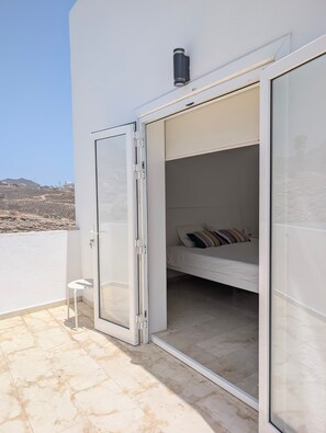 A balcony with a bed, a chair, and a view of the landscape.
