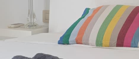 Una cama bien tendida con una almohada a rayas, una toalla enrollada y una lámpara sobre una mesita de noche.