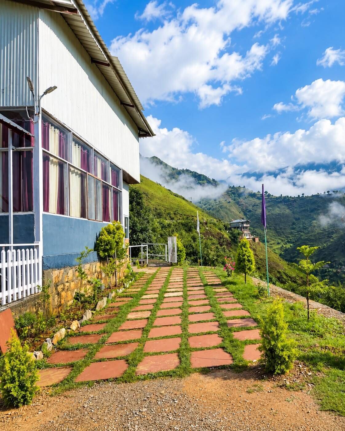 Un edificio con un sendero empedrado que conduce a un portón, rodeado de vegetación y colinas.