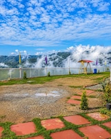 A garden with a red pathway, a swing set, and a view of mountains under a cloudy sky.