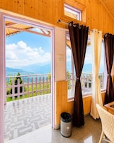 A wooden room with a balcony, a white fence, and a view of green hills.