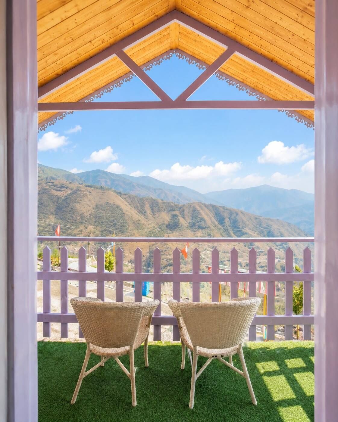Un espacio de estar techado al aire libre con dos sillones de mimbre y vistas a un paisaje montañoso.