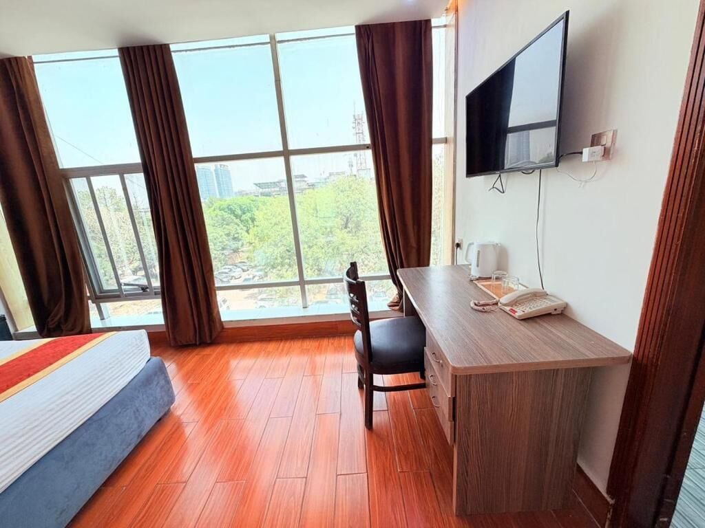 A hotel room with a bed, desk, chair, TV, and large windows.