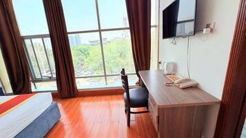 A hotel room with a bed, desk, chair, TV, and large windows.