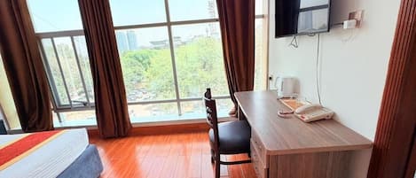 A hotel room with a bed, desk, chair, TV, and large windows.