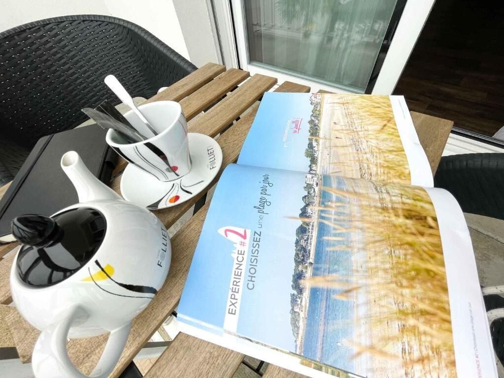 A table with a teapot, cups, and a brochure titled 'EXPERIENCE #2 CHOISISSEZ une plongée dans le joug.'