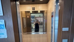 Un ascensor con pantalla digital, un cartel de prohibido fumar y un espejo que refleja el interior.