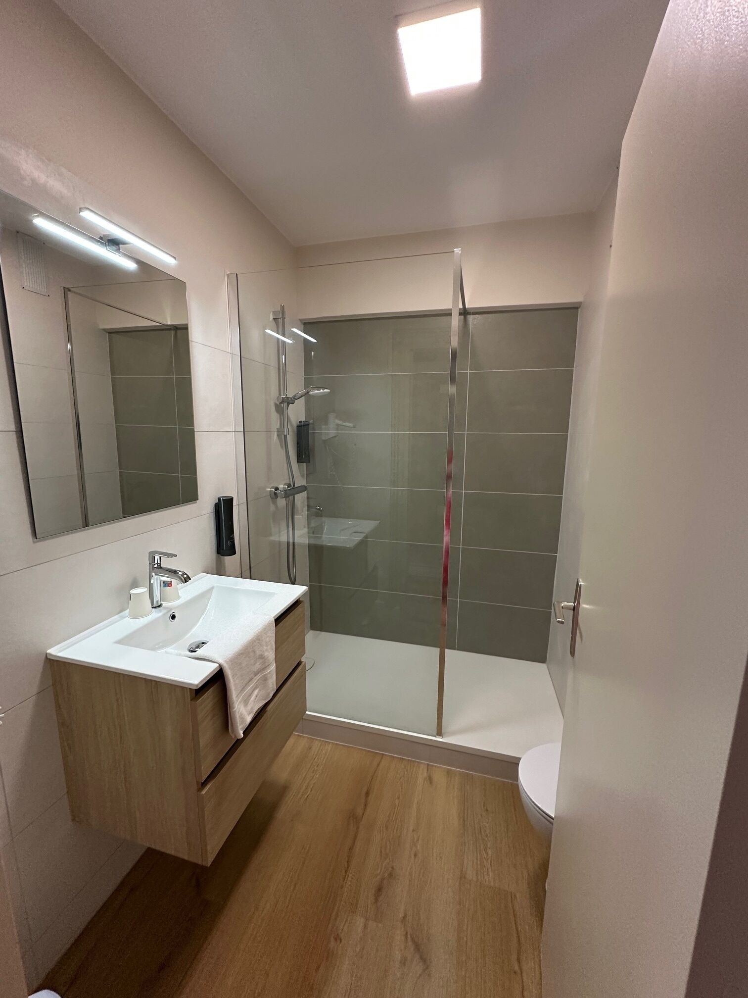 Une salle de bain moderne avec une douche à parois de verre, un lavabo blanc et un meuble-lavabo en bois.