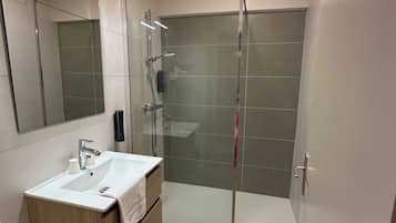 Une salle de bain moderne avec une douche à parois de verre, un lavabo blanc et un meuble-lavabo en bois.