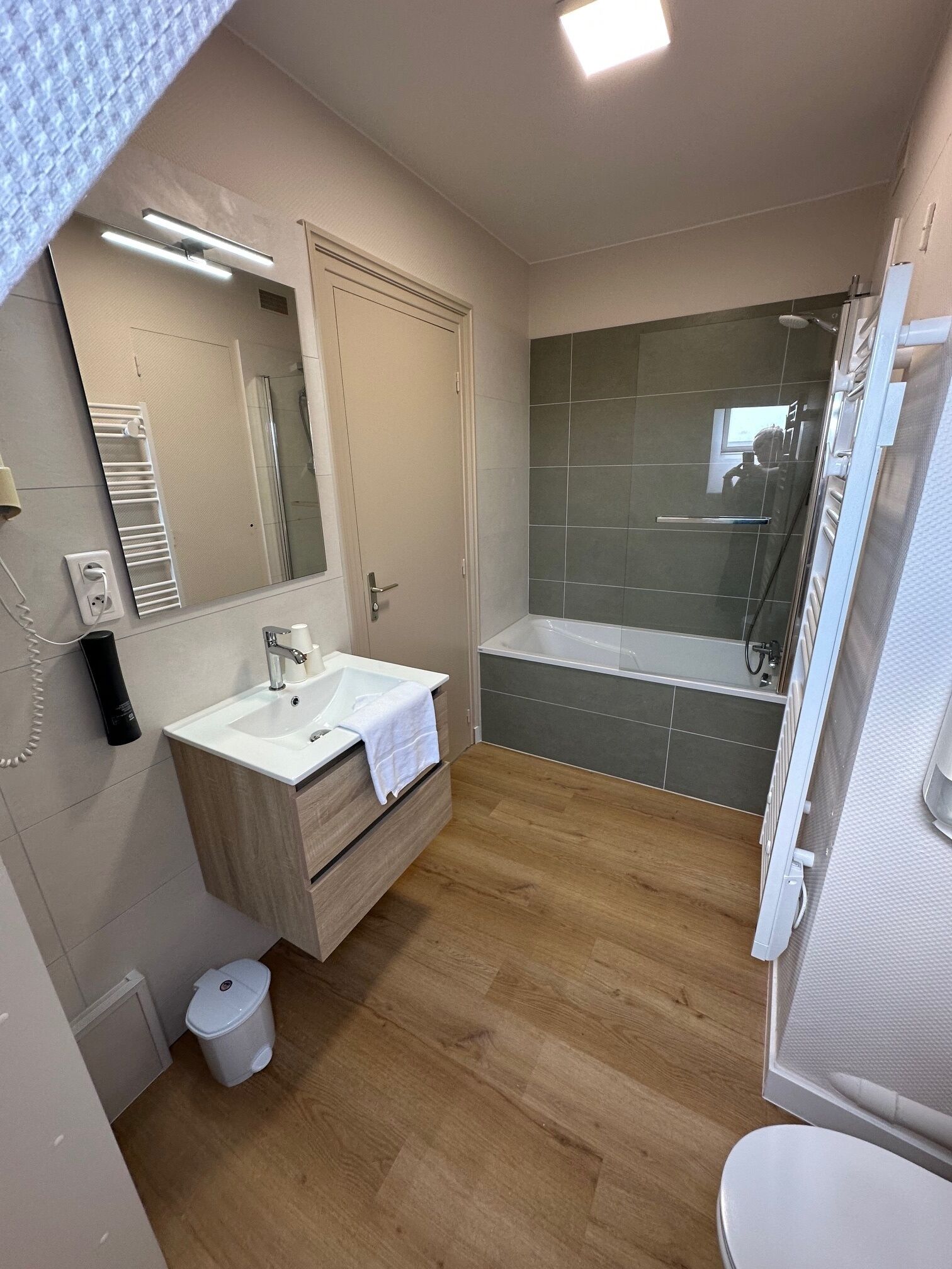 Un baño moderno con lavamanos blanco, espejo y cabina de ducha con mampara de vidrio.