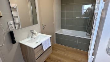 Un baño moderno con lavamanos blanco, espejo y cabina de ducha con mampara de vidrio.