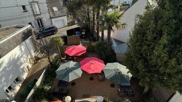 A courtyard with umbrellas, a palm tree, and buildings in the background.
