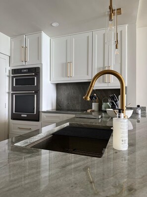 A modern kitchen with white cabinets, a black oven, and a gold faucet. - Oceanfront Gem • Newly Renovated (Miami Beach)