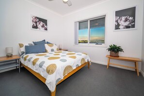 A bedroom with a bed, a window, a bedside table, a lamp, and a potted plant. - Gippsland Gem - 3/4 bedroom Accessible Accommodation (Yallourn North)