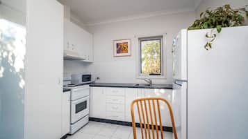 A kitchen with white cabinets, a microwave, a stove, a sink, and a window with a view of trees.