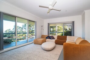 A modern living room with a large window, a ceiling fan, and a sectional sofa. - Gippsland Gem - 3/4 bedroom Accessible Accommodation (Yallourn North)