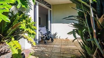 A wheelchair in a covered outdoor area with a tiled floor and large green plants.