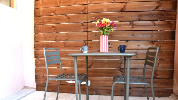 A small outdoor seating area with a table and two chairs, a striped vase with flowers, and a blue mug on the table. - Cozy Calade - Quiet, Self-Contained Studio with a Terrace - Downtown (Villefranche-sur-Saône)