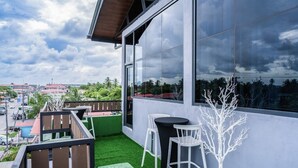 A balcony with a view of the city, a table, chairs, and artificial greenery. - Shelbees Suites - Garden Suite 202 (Cornelia Ida)