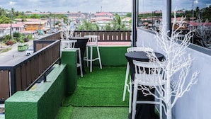 Une terrasse extérieure avec un revêtement de gazon synthétique, des chaises blanches et une sculpture d’arbre blanche.
