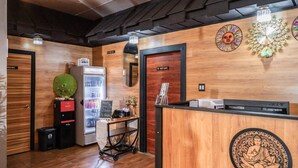 Un espace d’accueil comprenant un bureau en bois, un réfrigérateur, une machine à café et une horloge murale.