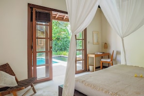 A bedroom with a bed, a chair, a desk, and a view of a swimming pool. - Villa Charlie Seminyak (Bali)