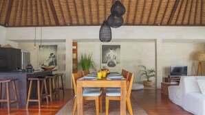 A dining area with a wooden table, chairs, and a woven mat. - Villa Charlie Seminyak (Bali)