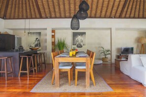 A dining area with a wooden table, chairs, and a woven mat. - Villa Charlie Seminyak (Bali)