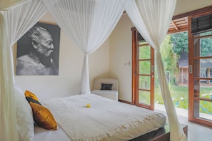 A bedroom with a bed, a bedside table, a chair, a window, and a door. - Villa Charlie Seminyak (Bali)